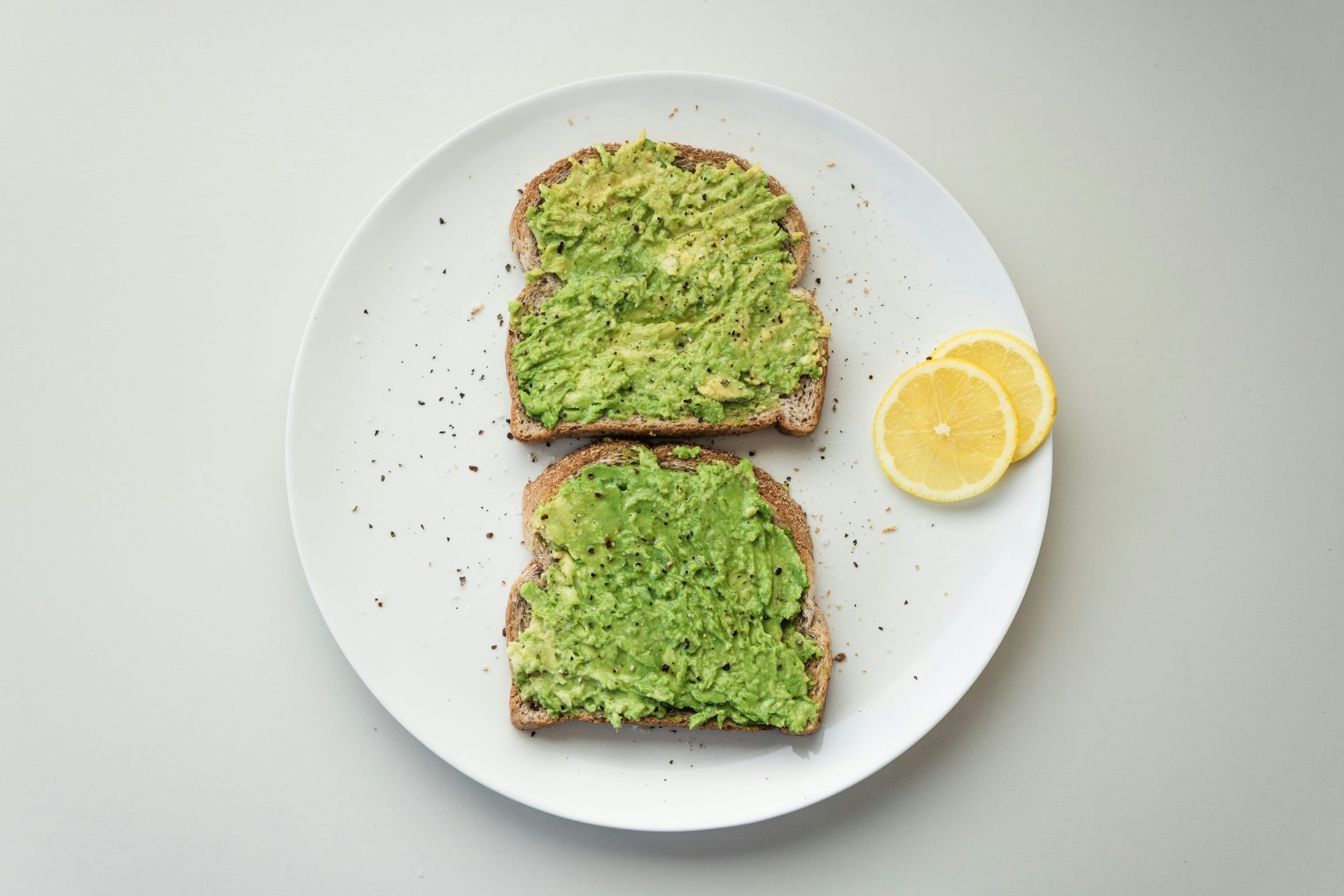 Avocado toast on white plate with lemon.